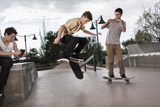 Teenage boys filming each other skateboarding in park