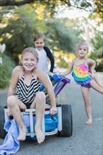 Children in swimsuits pushing cart on rural road