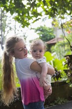 Caucasian girl carrying baby boy in tropical garden