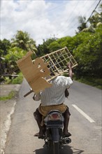 Man carrying wooden furniture on scooter