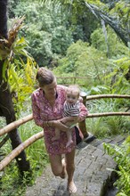 Caucasian mother carrying baby up steps in jungle landscape