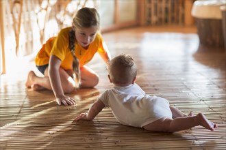 Caucasian girl and baby sibling playing on floor