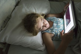Caucasian girl using tablet computer in bed