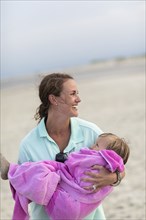 Caucasian mother carrying daughter on beach