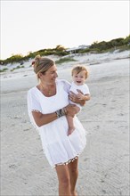 Caucasian mother carrying baby on beach