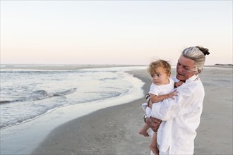 Caucasian woman carrying grandson on beach