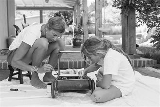 Caucasian mother and daughter painting toy on porch