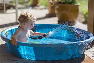 Caucasian baby playing with hose in wading pool