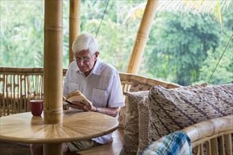 Older Caucasian man reading in bamboo living room