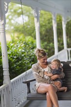 Caucasian mother and toddler sitting in swing on porch