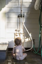 Nude Caucasian toddler playing with hose