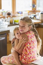Caucasian girl holding toddler brother in kitchen