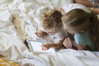 Caucasian girl and toddler brother using tablet computer on bed