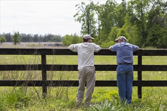 Caucasian father and son leaning on fence by rural field