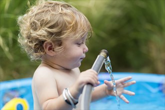 Caucasian baby boy playing with hose in swimming pool