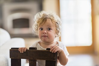 Caucasian baby boy standing behind chair in living room