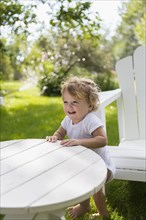 Caucasian baby boy standing at table in backyard