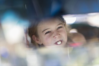 Reflection of Caucasian girl blowing bubble gum bubble in rearview mirror