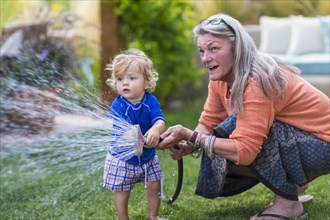 Caucasian grandmother and baby grandson watering lawn with hose