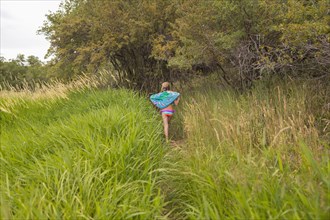 Caucasian girl carrying towel in tall grass