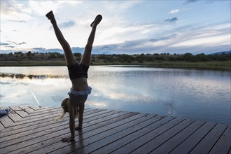 Caucasian girl doing handstand on wooden deck near lake
