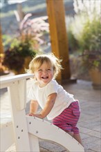 Caucasian baby boy climbing adirondack chair on patio