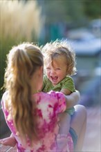 Caucasian sister holding laughing baby brother outdoors