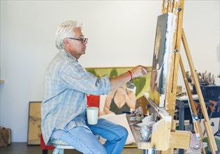 Older Hispanic artist painting in studio