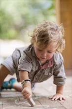 Caucasian baby boy drawing with chalk on brick patio