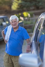 Senior Caucasian man leaning against car