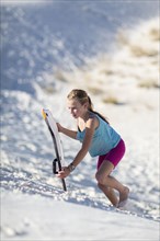 Caucasian girl climbing sand dune with sled