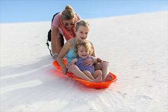 Caucasian mother and children sledding on sand dune
