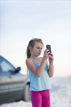 Caucasian girl taking cell phone photograph near car