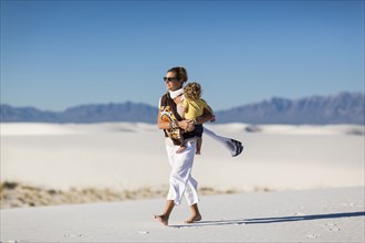 Caucasian mother carrying son on sand dune