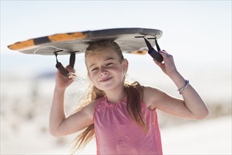 Caucasian girl carrying sled on sand dune