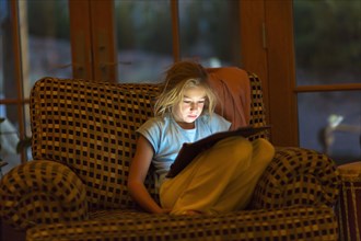 Caucasian girl using digital tablet in armchair at night
