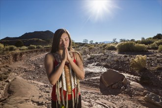 Mixed race woman praying in remote desert landscape