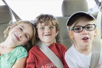 Caucasian children smiling in back seat of car