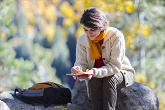 Mixed race woman reading journal on rock