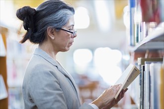 Older Hispanic woman reading book in library