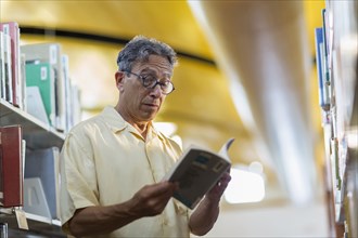 Older Caucasian man reading book in library