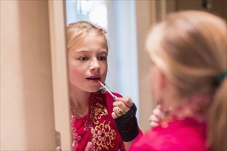 Caucasian girl applying lip gloss in mirror