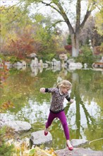 Caucasian girl jumping on rocks in pond