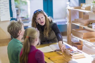 Caucasian Montessori teacher helping students in classroom