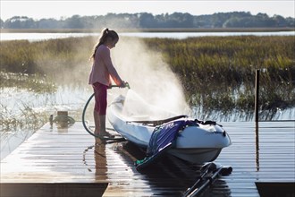Caucasian girl spraying canoe on wooden dock over lake