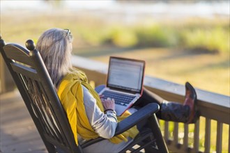 Older Caucasian woman using laptop on porch