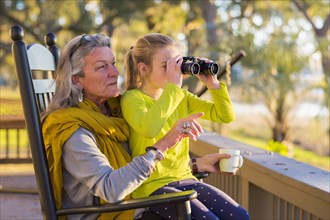Caucasian grandmother and granddaughter using binoculars on porch