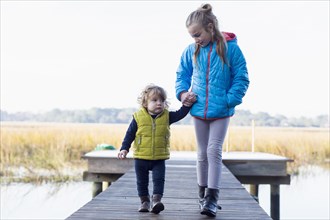 Caucasian brother and sister walking on wooden dock