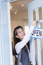 Hispanic small business owner hanging open sign on door