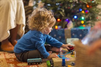 Caucasian baby boy playing with toys under Christmas tree
